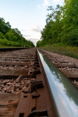 Bulutlu bir günbatımında çekilen yeşilliklerle çevrili trenin güzel bir manzarası ufukta beliriyor. Eden Prairie, Minnesota 'daki Birch Island Park' ta çekilmiş kaliteli bir fotoğraf..