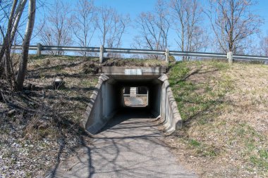 İlkbaharın başlarında bir korkuluk ve çıplak ağaçlar tarafından çerçevelenmiş bir yaya tüneli bir yolun altından geçer. Sahne huzur ve yalnızlığı çağrıştırıyor, kıştan bahara geçişi gösteriyor..