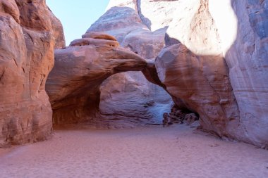 Utah, Arches Ulusal Parkı 'nda muhteşem bir kumtaşı kemeri. Etrafı pürüzsüz kırmızı kaya oluşumları ve yumuşak kumlu arazilerle çevrili. Temiz bir çöl gökyüzünden gelen sıcak doğal ışıkla yıkanmış..