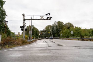 Yağmurlu bir günde Washington 'da arka planda bir köprüyle demiryolu geçidi. Islak asfalt ve bulutlu gökyüzü, bölgenin karakteristik havasını vurgulayan dengesiz bir atmosfer yaratıyor..