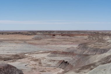 Arizona, Petrified Forest Ulusal Parkı 'ndaki Mavi Orman Yürüyüşü boyunca uzanan kurak ve katmanlı arazinin geniş bir görüntüsü eşsiz jeolojik oluşumları ve geniş çöl manzaralarını vurguluyor..