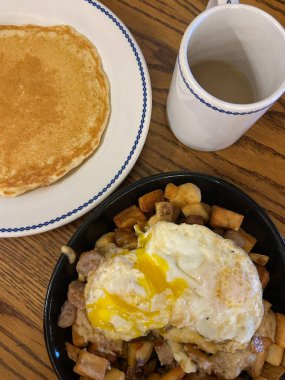 Arizona, Grand Canyon Ulusal Parkı 'ndaki ahşap bir masada krep ve bir kupa kahvenin yanında kızarmış yumurta, patates ve sosis servis edilen doyurucu bir kahvaltı tavası..