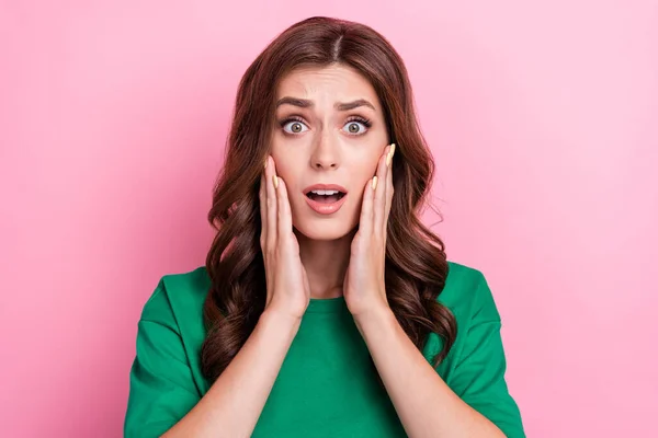 Photo of gorgeous scared astonished girl with wavy hairdo dressed green t-shirt palms on cheekbones isolated on pink color background.