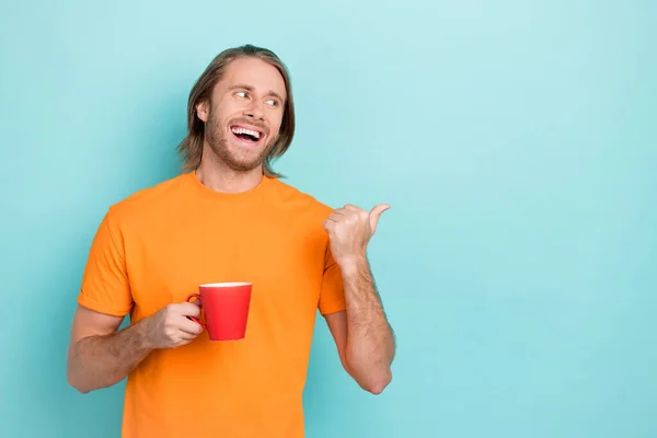 照片上快乐而积极的男人穿着橙色的T恤喝咖啡看着手指空空荡荡的空间孤立的茶色背景 — 图库照片
