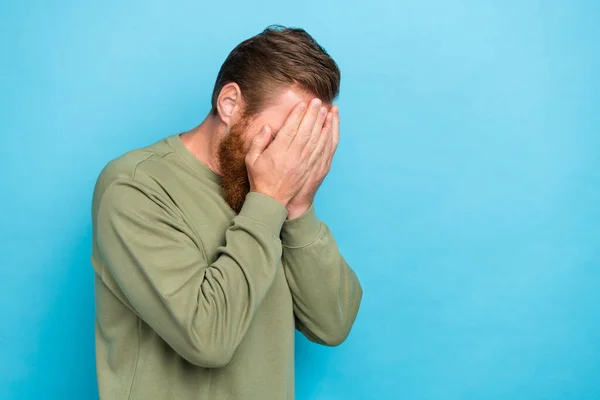 Portrait of sad upset unhappy guy with ginger hairdo dressed khaki pullover palms cover face cry isolated on turquoise color background.