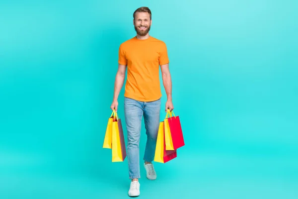 全长尺寸的照片 穿着橙色T恤衫的英俊男子拿着购物袋买新衣服 衣服都是用单调的色彩背景隔开的 — 图库照片