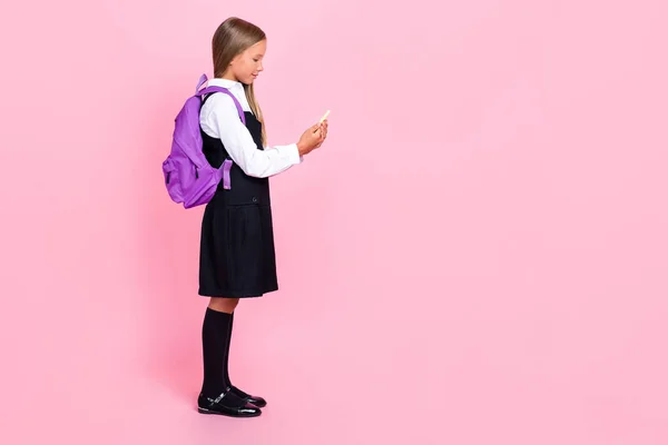 全长侧面轮廓照片聪明的积极女孩 金发碧眼 身穿制服 看着智能手机被粉色背景隔离 — 图库照片