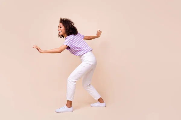 Full length photo of positive carefree girl striped t-shirt white trousers sneaking look empty space isolated on beige color background.