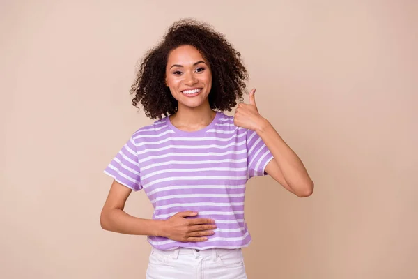 かわいい女性の写真は 紫色のTシャツを着て親指を表示腕の胃孤立ベージュ色の背景 — ストック写真