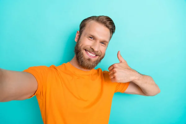 承認の写真楽観的な男ブロンドヘアスタイルオレンジ色のTシャツを着て親指アップします自慰行為をします絶縁上のティール色の背景 — ストック写真