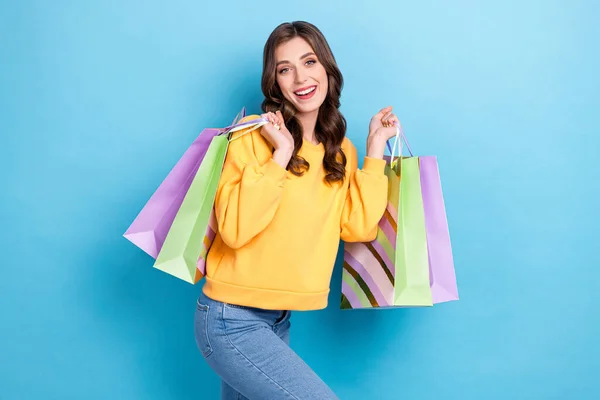 魅力的な若い女の子の写真の肖像はショッピングバッグを運ぶ楽しむ週末服スタイリッシュな黄色の服は青の色の背景に孤立 — ストック写真