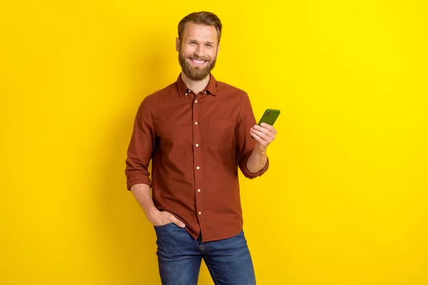 男性的な髭を持つ楽観的なハンサムな男の肖像 バーガンディシャツは黄色の色の背景に隔離されたポケットに携帯電話の手を保持 — ストック写真