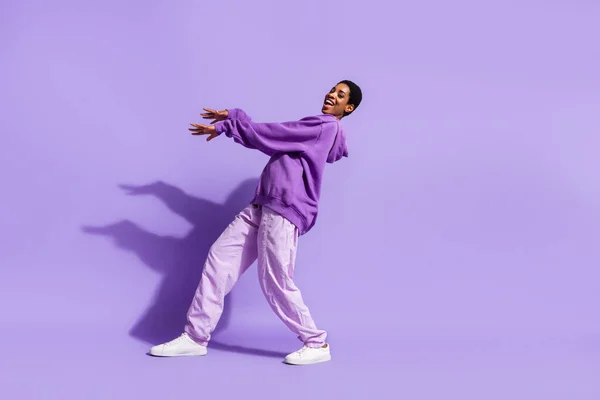 全长照片 年轻女子跳舞时穿着与紫色背景隔离的连帽裤鞋 — 图库照片
