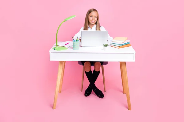フルサイズ写真の良い気分楽観的な女子高生とともにブロンド髪身に着けている学校制服座る上の机の上にピンク色の背景 — ストック写真