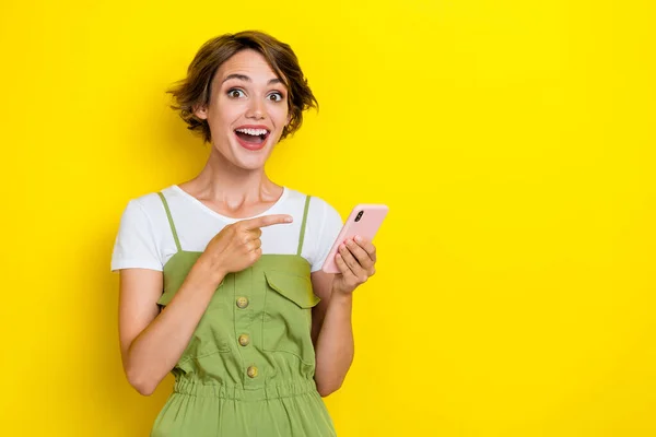 若いクレイジー女性の写真は カーキ全体的な驚きの指ポイント新しいスマートフォンを身に着けています日付黄色の色の背景に隔離されたアプリ — ストック写真