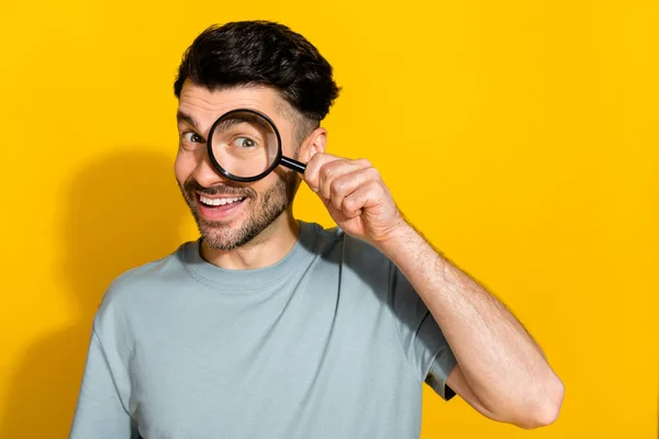 Photo of cheerful satisfied man stylish clothes using magnifying glass find investigation empty space isolated on yellow color background.
