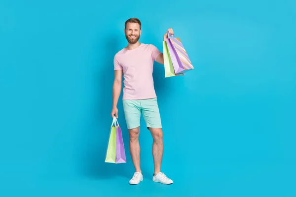 全长尺寸的英俊年轻人的照片享受周末举行购物袋穿着时髦的粉红色衣服与青色背景隔离 — 图库照片