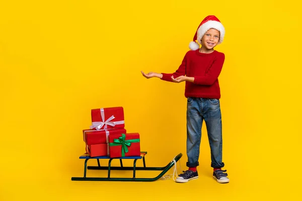 stock image Full length photo of cute little boy palms hold empty space stack gifts sledge wear trendy red garment isolated on yellow color background.