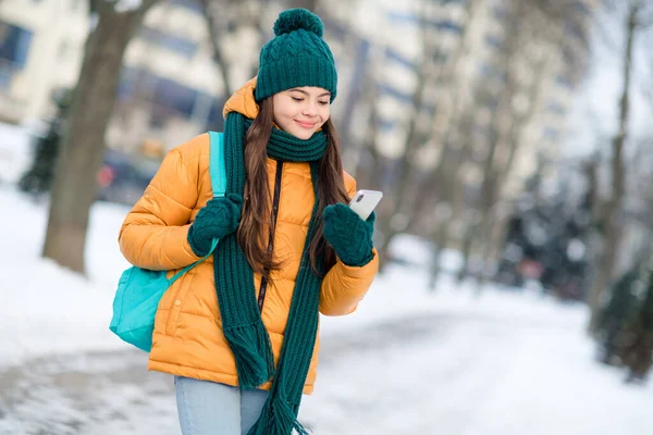 stock image Portrait of attractive cheerful preteen girl using device watching video smm post strolling on fresh air snowy weather outdoors.