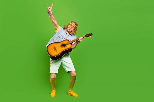 写真の若者の演奏ギター作り角付きシンボルはデニムジーンズベストショートパンツ隔離された明るい色の背景を着用 — ストック写真