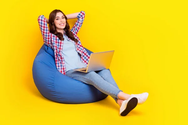 Full length photo of satisfied woman sitting relaxed beanbag nap chill after working programmer new netbook isolated on yellow color background.