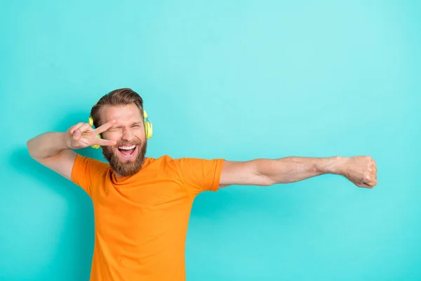 Photo of crazy beard guy listen music dance wear headphones orange t-shirt isolated on turquoise color backgroiund.