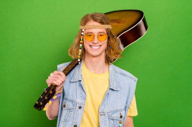 Portrait of attractive cheerful guy carrying guitar rest weekend holiday isolated over bright green color background. clipart