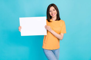 Portrait of nice cute adorable woman with long hairstyle dressed yellow t-shirt hold white banner isolated on blue color background. clipart