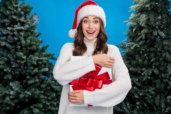 Photo of sweet excited lady wear santa claus helper hat hugging xmas presnt isolated blue color background.
