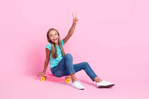 興奮したかなり小さな子供の完全な長さの写真は Vサイン空のスペース孤立ピンク色の背景を示すターコイズTシャツに乗るスケートボードを着用 — ストック写真
