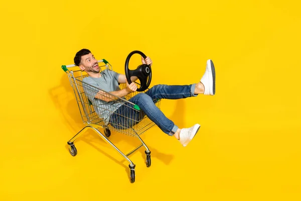 兴奋积极的男人坐在市场小推车上手握方向盘 看起来空荡荡的 用黄色背景隔开的空间 — 图库照片