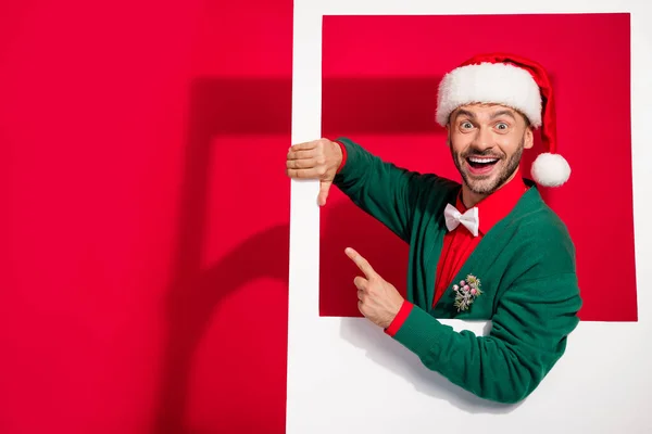 Photo of excited pretty guy dressed xmas green cardigan holding photo frame pointing empty space isolated red color background.
