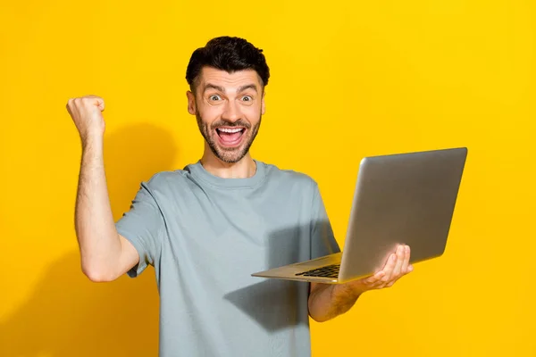 年轻而兴奋的毛茸茸的男人拍出的肖像照片 拍出了积极的情绪 庆祝心情好 拿着笔记本电脑 在黄色背景下提供绝配 — 图库照片