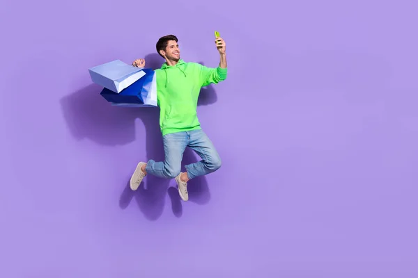 Full length photo of positive man wear green rising bargains jumping recording video vlog empty space isolated purple color background.