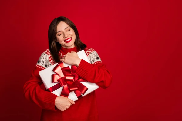 Portrait of thankful funny positive woman bob hairdo dressed red sweater hug present box eyes closed isolated on red color background.