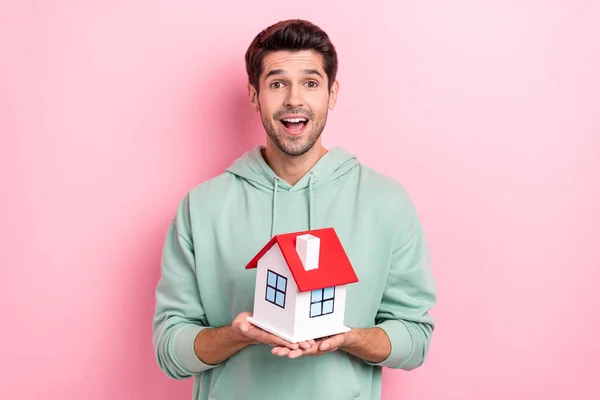 Portrait of astonished cheerful man hands hold small house open mouth isolated on pink color background.