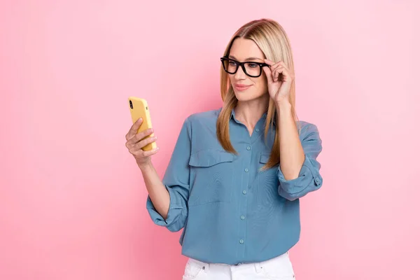 若い正のプロのブロガーの女性の写真は ピンクの色の背景に隔離された新しい情報素敵な眼鏡を閲覧スマートフォンを保持します — ストック写真