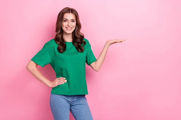 楽観的な豪華な女の子の肖像波状のヘアドアはピンクの色の背景に隔離された空のスペースを示す腰の上に緑のTシャツの手を着用 — ストック写真