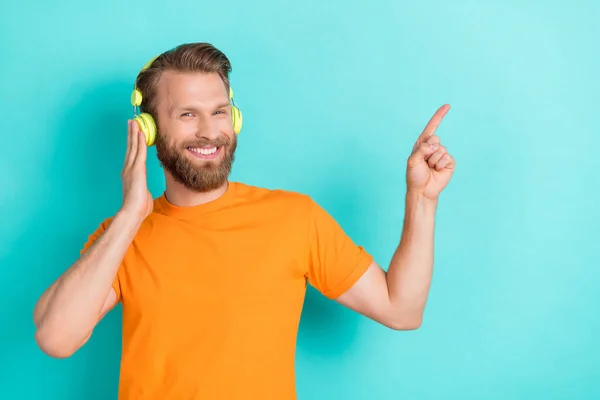 stock image Photo of cheerful positive optimistic man dressed orange t-shirt indicating empty space touch headphones isolated on teal color background.