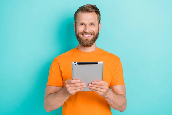 乐观的胡子男人拿着平板电脑 穿着橙色的T恤衫 在茶色的衬托下隔离开来 — 图库照片