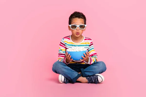 可愛い印象の少年のフルサイズの写真縞模様の長袖ジーンズ座っているホールドポップコーンボウルピンク色の背景に隔離 — ストック写真