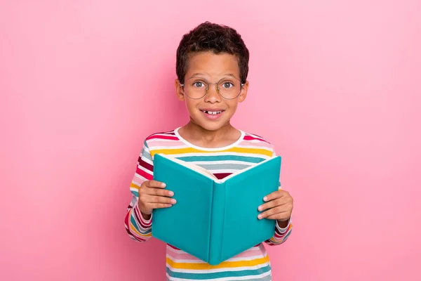 可爱的正面形象给小学生留下深刻印象的波浪形头发 穿着条纹长袖衫 拿着一本粉红色背景的书 — 图库照片