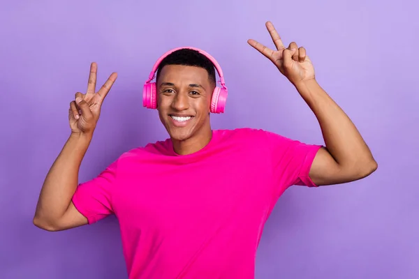 Photo of handsome satisfied friendly guy box haircut dressed pink t-shirt headphones showing v-sign isolated on purple color background.