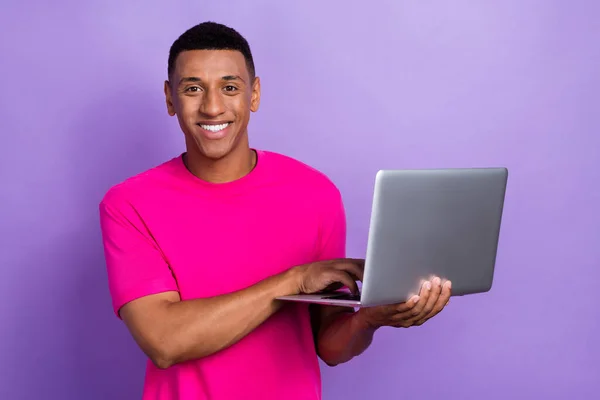 stock image Photo of positive cheerful satisfied guy with box haircut dressed pink t-shirt typing on laptop isolated on purple color background.