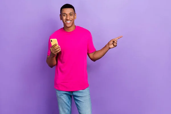 明るいハンサムな男の箱の髪型の写真ピンクのTシャツを着て携帯電話を持っている紫色の背景に隔離された空のスペースを演出 — ストック写真