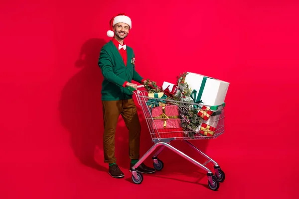 Full length photo of cute man wear x-mas green cardigan buying tray noel presents bargains isolated red color background.