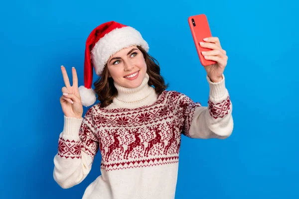 Photo of charming lady wear ugly sweater use social media app make self picture video record v-sign isolated on blue color background.