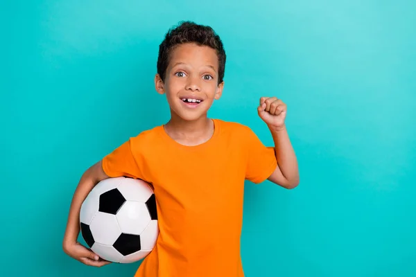 写真の甘い運の良い小さな男の服を着てオレンジTシャツキャッチサッカーボール上昇拳孤立したティール色の背景 — ストック写真