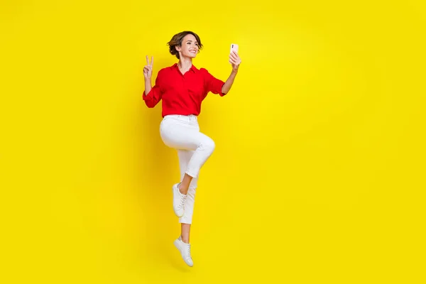 フルサイズポートレートのエネルギー魅力的な女の子ジャンプデモンストレーションV Sign作る自画を黄色の色の背景に隔離 — ストック写真