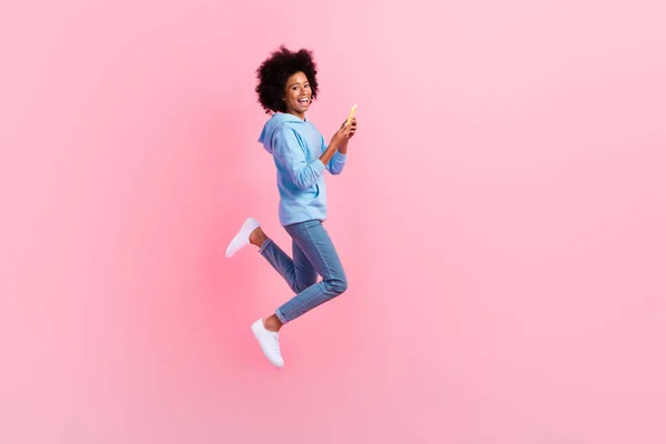 興奮した小さな女子高生ジャンプホールド使用電話絶縁上のピンク色の背景 — ストック写真